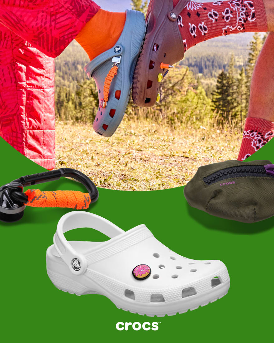Two people "high fiving" their Crocs with adventure Jibbitz accessories in the foreground, with a classic White clog.