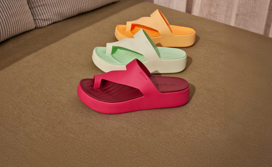 Colorful Crocs sandals on a brown surface with palm trees in background