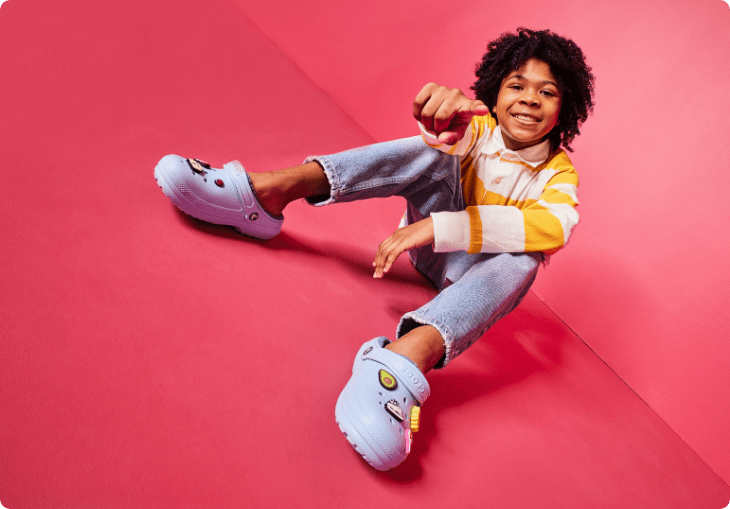 Child pointing posing wearing crocs, pointing at camera.