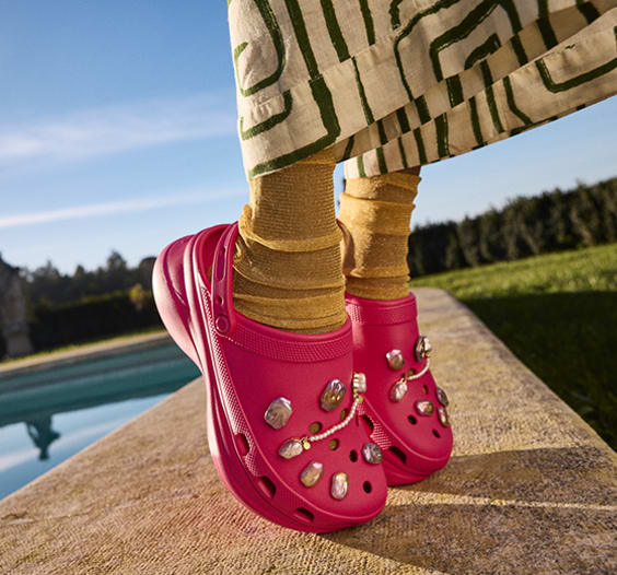 Legs of girl wearing funky pants and gold tights standing on tippy toes in hot pink platform crocs with silver pearl jibbitz