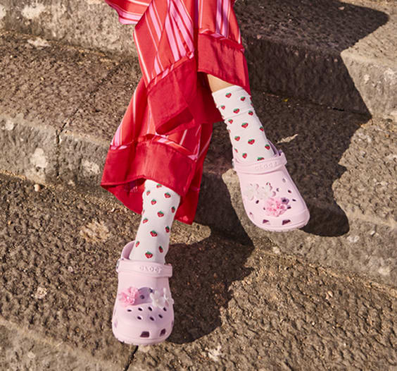 Legs of girl wearing funky red pants with strawberry socks and pink crocs with flower jibbitz