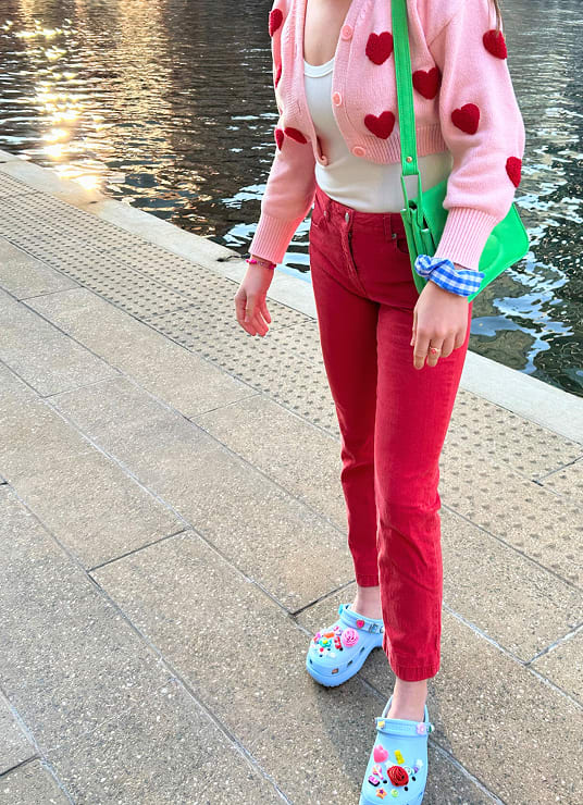 Girl wearing heart sweater, red pants and bright-blue platform crocs with loud and colorful jibbitz