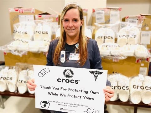 Healthcare Worker Holding sign thanking Crocs in front of donated Crocs.