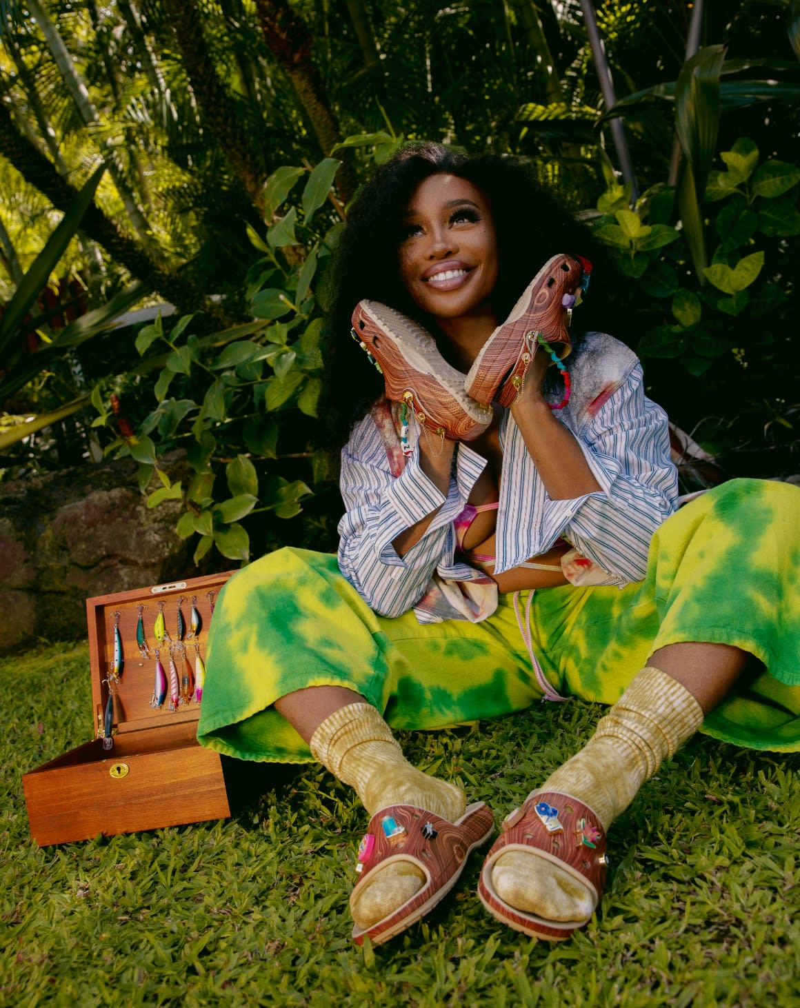 Sza posing in natural setting wearing Wood Print Clogs on hands, and Wood Print Slides on Feet.
