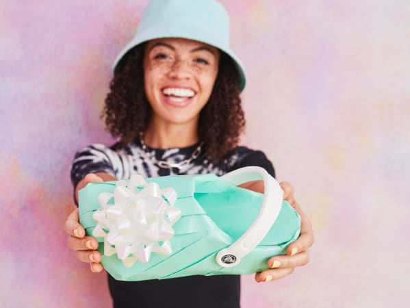 Femme tenant une chaussure Croc dans un paquet cadeau.